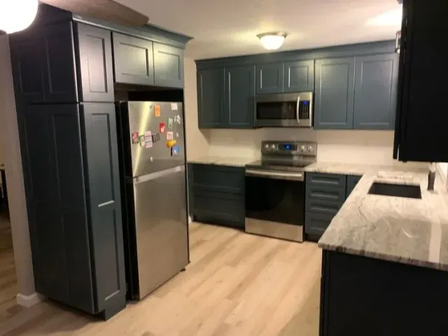 Blue kitchen cabinets and stainless steel appliances in a bright kitchen with light wood flooring.