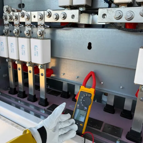 Close-up of electrical components inside a panel, with a hand holding a digital multimeter testing the circuit.