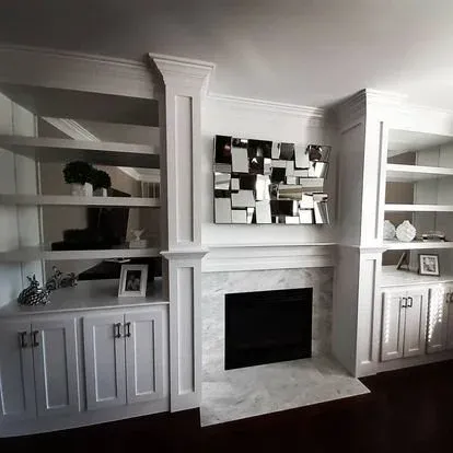 Living room with white built-in shelves on both sides of a fireplace, adorned with decorative items and picture frames, and a large mirror above the fireplace.