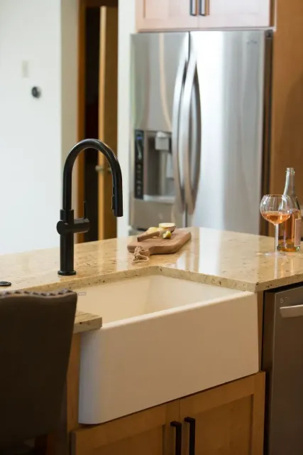 Kitchen sink and faucet on a countertop, with a stainless steel refrigerator in the background.