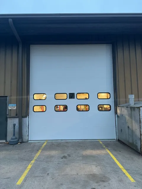 A white garage door with a lot of windows is sitting in front of a building.