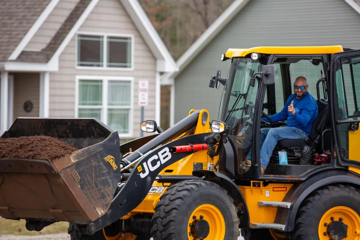 man inside bulldozer/excavator lifting dirt wearing blue shirt and sunglasses