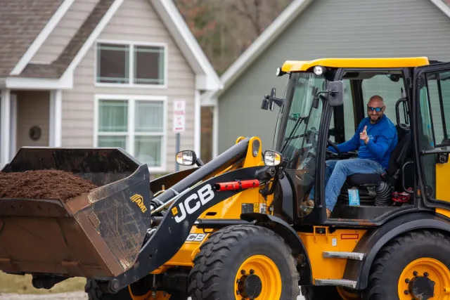 man inside bulldozer/excavator lifting dirt wearing blue shirt and sunglasses