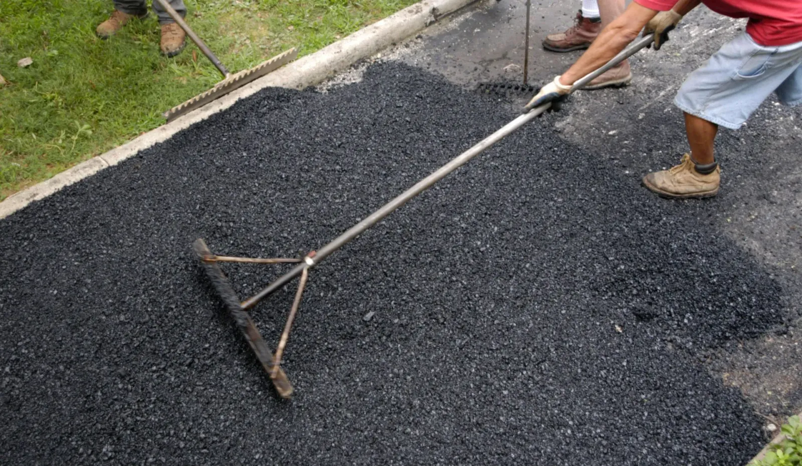 Workers spreading asphalt on a driveway with rakes.