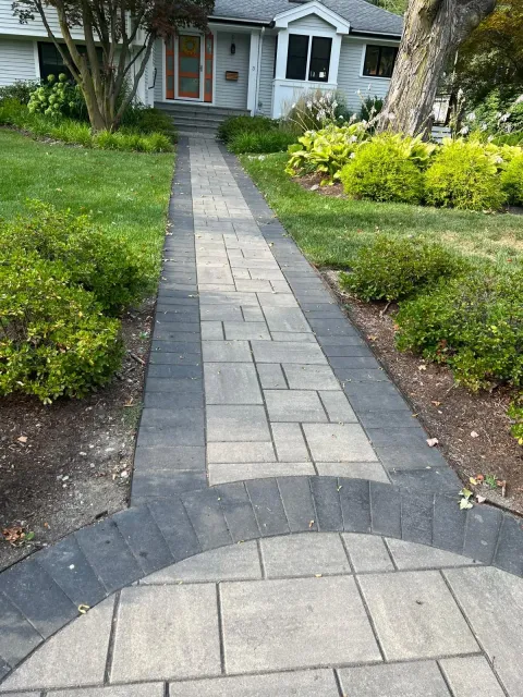 Stone walkway leading through a green front yard to a house with a red door