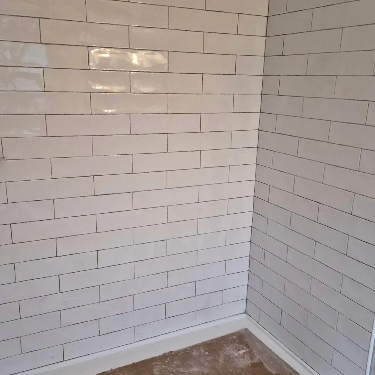 Corner of a room with white subway tile walls and a baseboard, with partially visible unpolished concrete floor.
