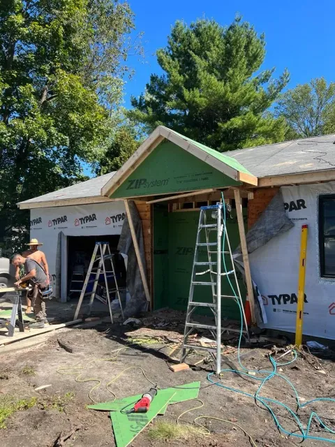 Construction workers frame a new entryway over a building entrance covered in green sheathing and white house wrap.