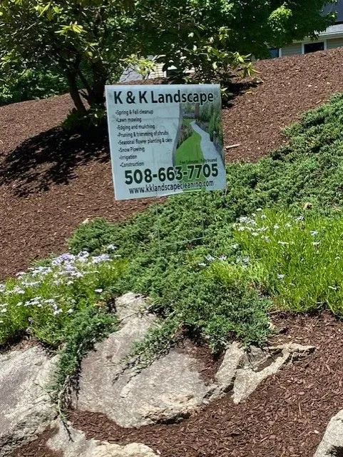 K & K Landscape sign in a landscaped yard with rock and mulch. Sign lists services and phone number.