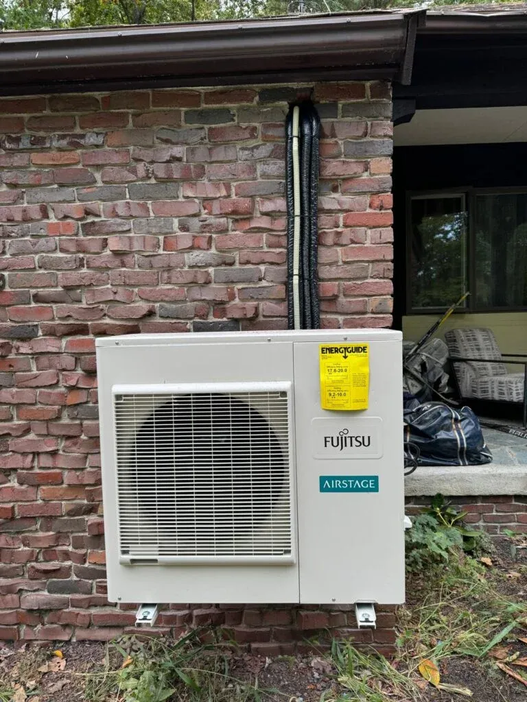 Newly installed Fujitsu Airstage outdoor heat pump unit mounted on a brick exterior wall