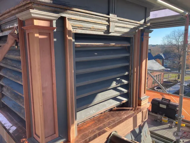 A wooden building with a copper roof and a window with shutters on it.