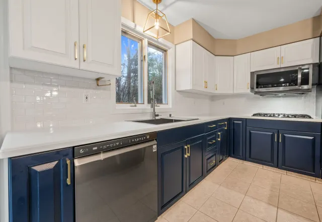 A modern kitchen featuring navy blue lower cabinets, white upper cabinets, white countertops, and stainless steel appliances.