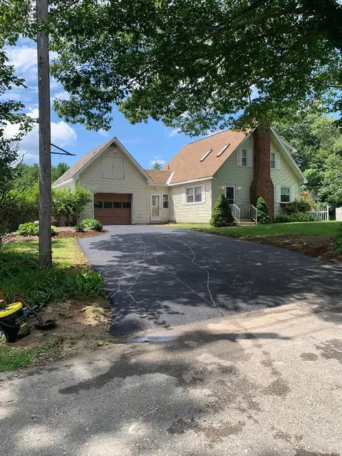 A large house with a driveway leading to it is surrounded by trees.