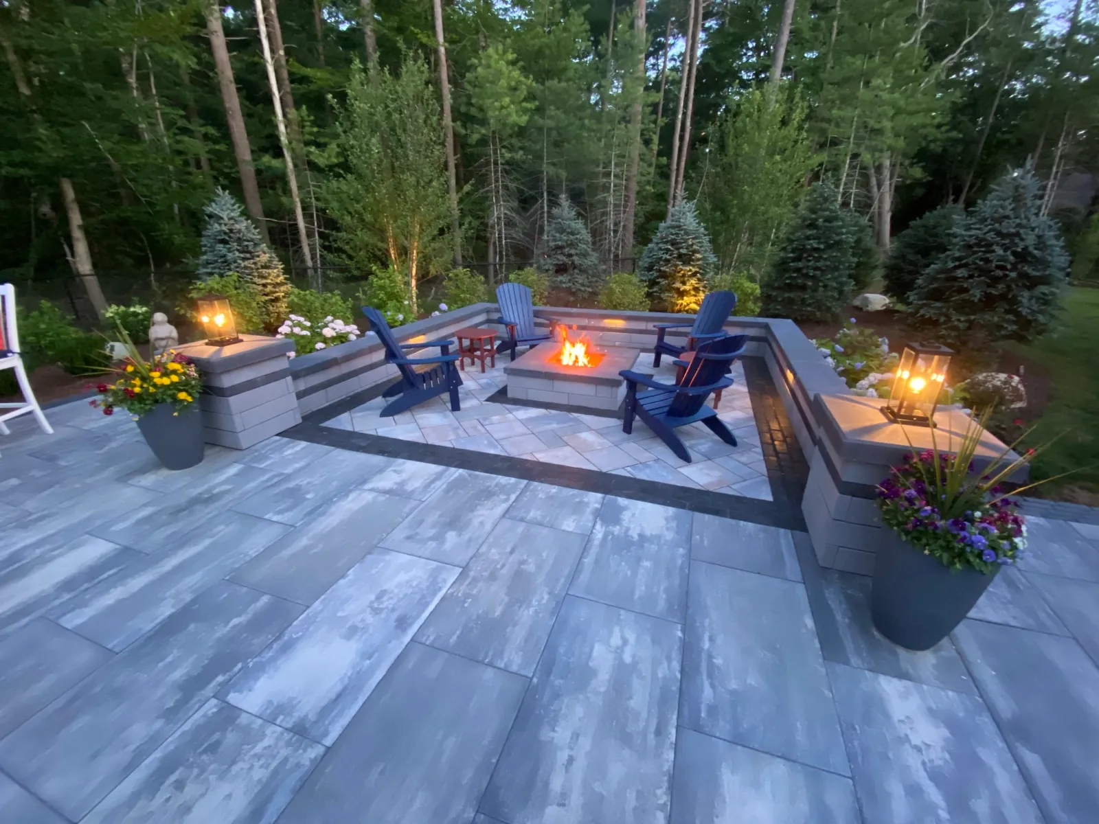 A stone patio with fire pit, outdoor lighting, and plantings