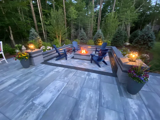 A stone patio with fire pit, outdoor lighting, and plantings