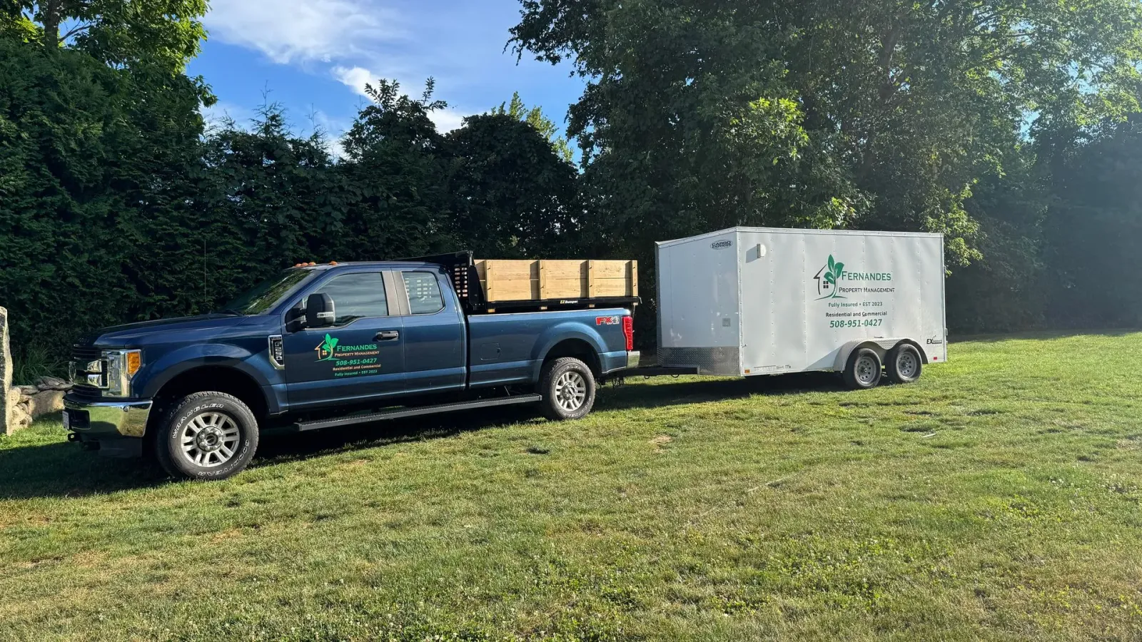 Blue pickup truck with trailer on grass, likely for landscaping services.