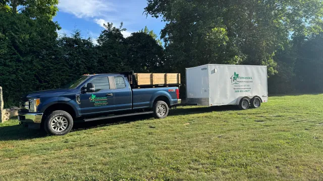 Blue pickup truck with trailer on grass, likely for landscaping services.