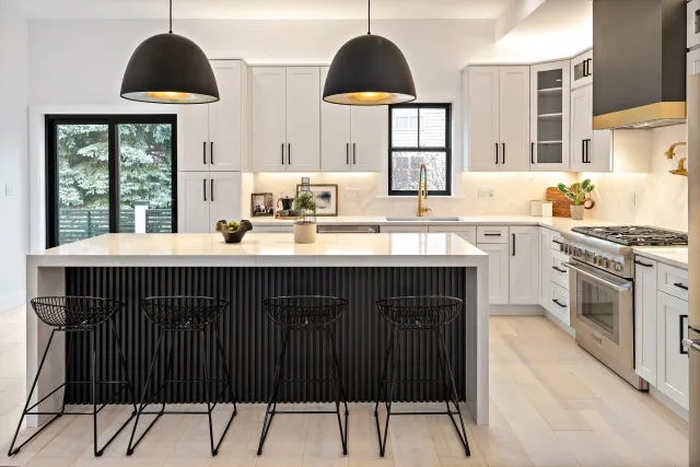 Modern kitchen interior with white and black color scheme featuring two large black hanging lights, three island stools an...