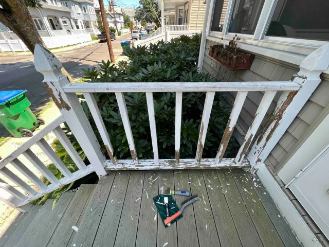 A side rail of a front porch in the process of being scraped and sanded