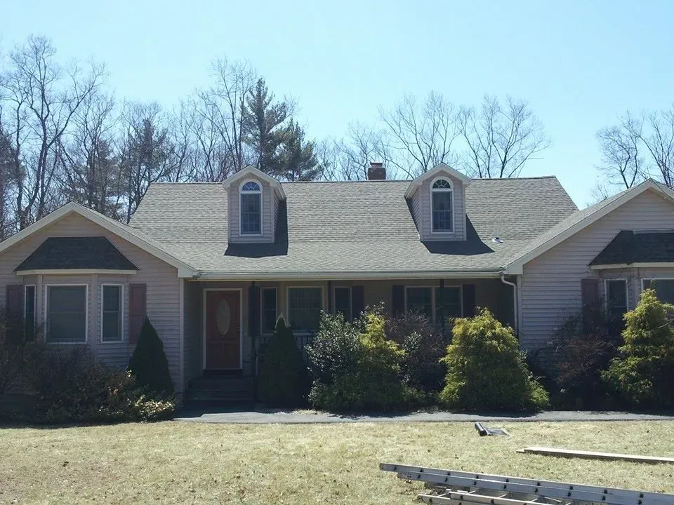 Beige ranch-style house with dormers, trees, and front yard.