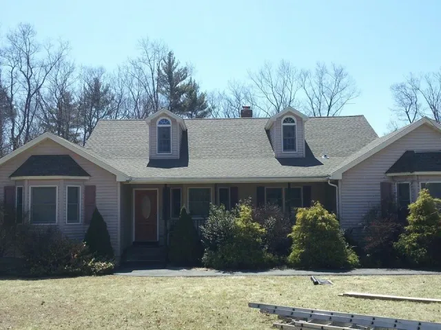 Beige ranch-style house with dormers, trees, and front yard.