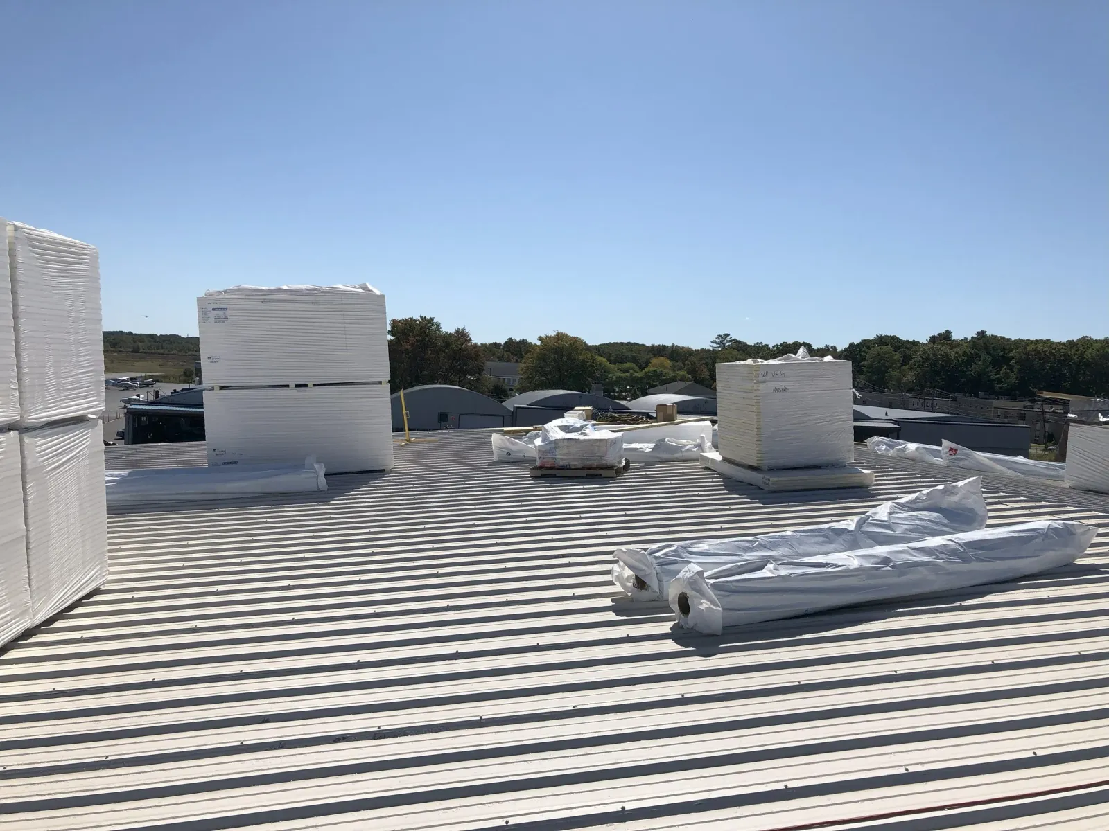 View of a metal rooftop with large stacks of insulated white roofing panels waiting to be put in place by WP Walsh Roofing of Massachusetts.