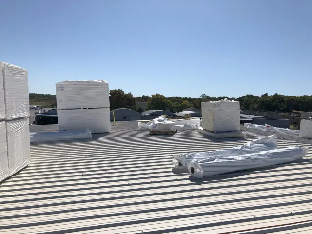 View of a metal rooftop with large stacks of insulated white roofing panels waiting to be put in place by WP Walsh Roofing of Massachusetts.