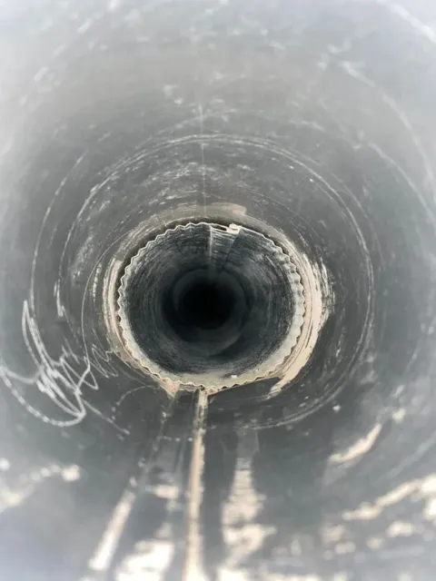 Inside a dark, cylindrical pipe. White, dried residue lines the inside.