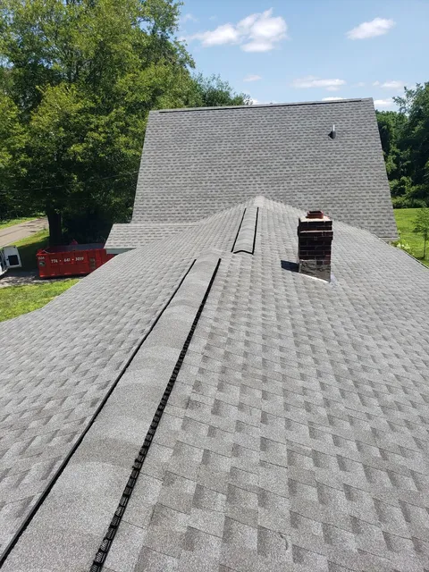 New asphalt shingle roof installation on residential home with chimney and ridge vents