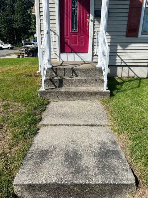 A concrete walkway leading to a red door of a house.