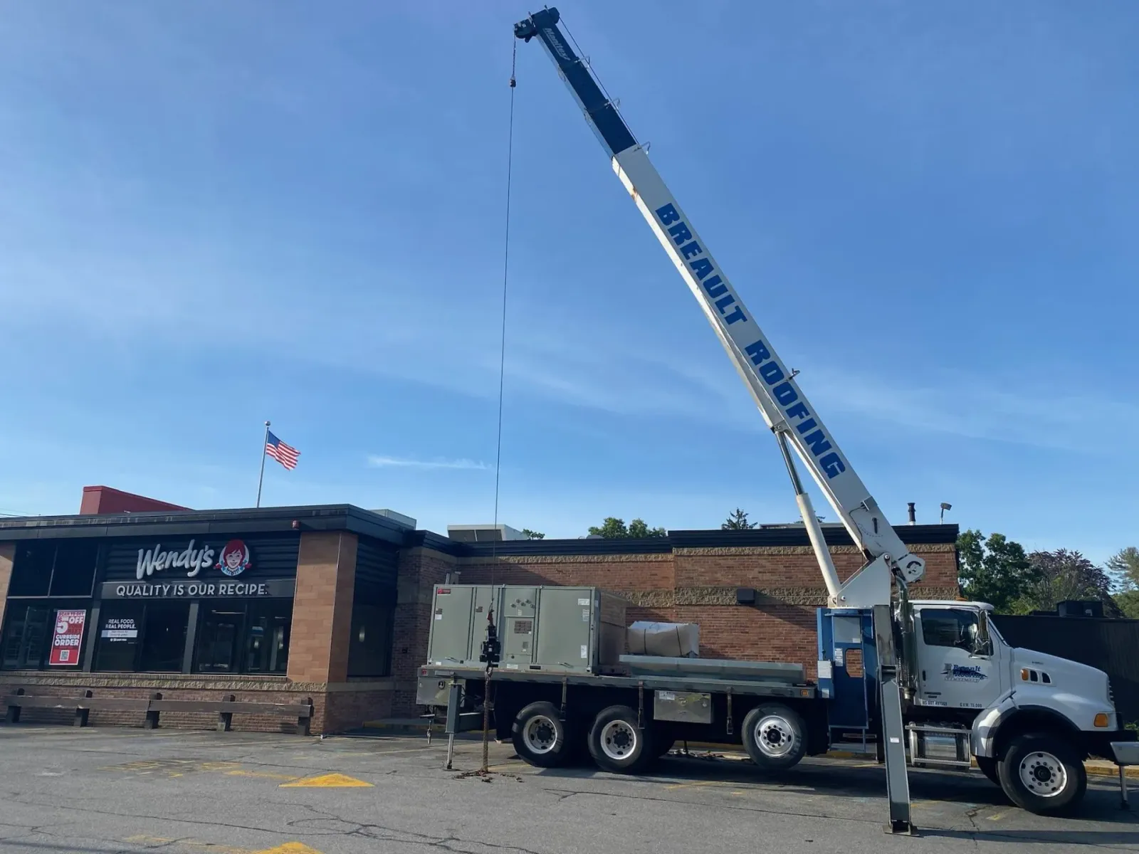 Crane truck lifting materials near a Wendy's restaurant under a blue sky.