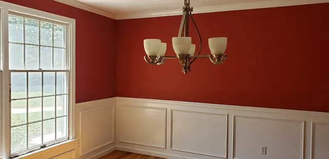 An empty dining room with red walls and a chandelier hanging from the ceiling.