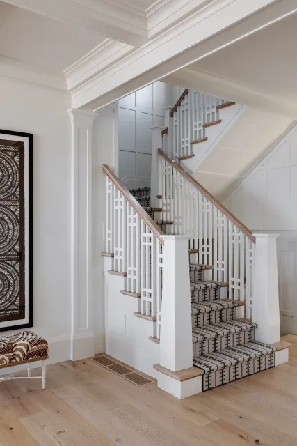 Hardwood floor refinishing in a Pembroke home with an interior staircase featuring white railings, a wooden handrail, carpeted steps, and framed artwork on the wall.