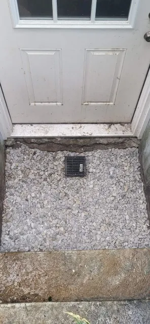 A white door with a drain on the ground next to it