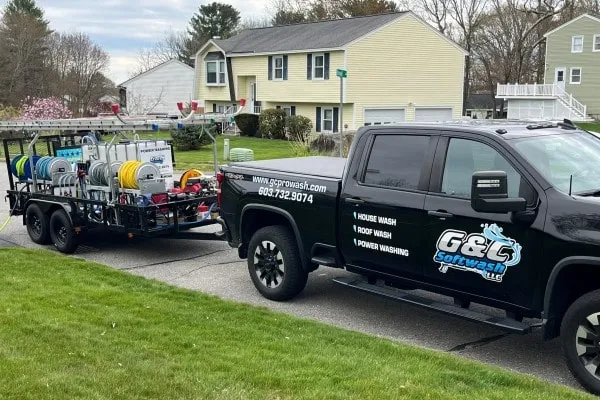 G&C Softwash LLC truck and trailer with power washing equipment parked on a residential street, ready for a house wash. The yellow house in the background suggests a typical home cleaning project.