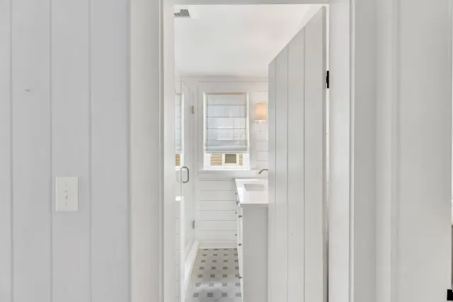 View through a white doorway into a bright bathroom with a sink, window, and patterned tile floor
