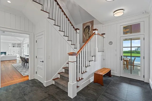 Entryway with stairs, bench, and door to patio. White walls, dark floor, and natural wood accents.