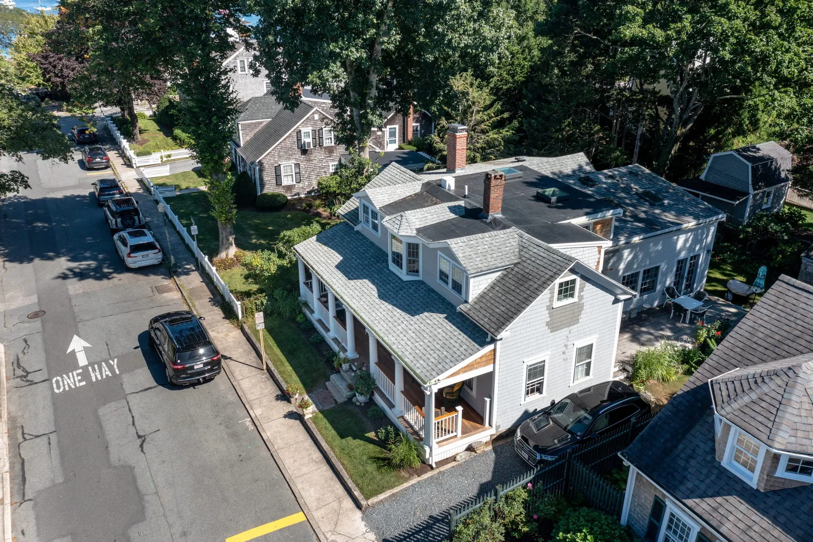 Aerial view of a residential neighborhood in Massachusetts featuring a stylish gray house with a front porch, surrounded by well-maintained lawns and parked cars, illustrating the quality of home renovations by Harding Builders.