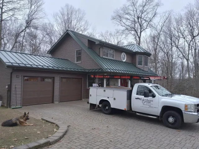 White utility truck parked outside a rustic house with garage, under a gray sky.