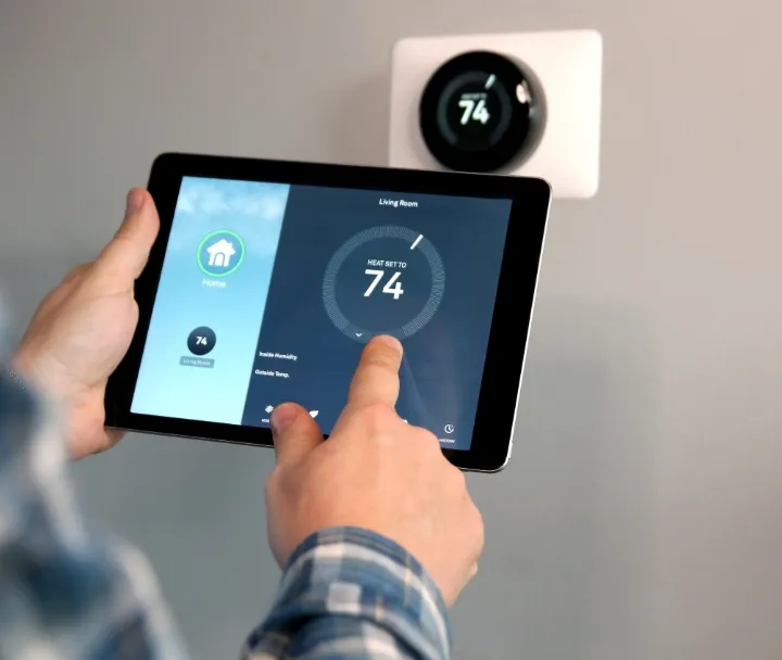 Person using tablet to control smart thermostat displaying 74 degrees in modern home
