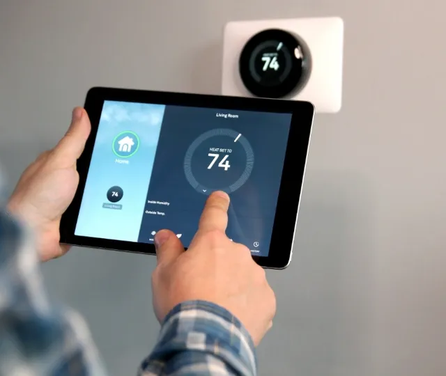 Person using tablet to control smart thermostat displaying 74 degrees in modern home
