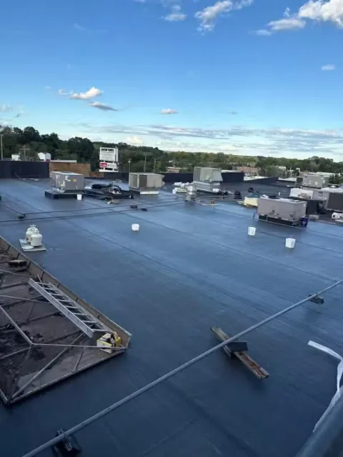 View of a commercial building's flat roof with HVAC units, vents, and a ladder, under a partly cloudy sky.