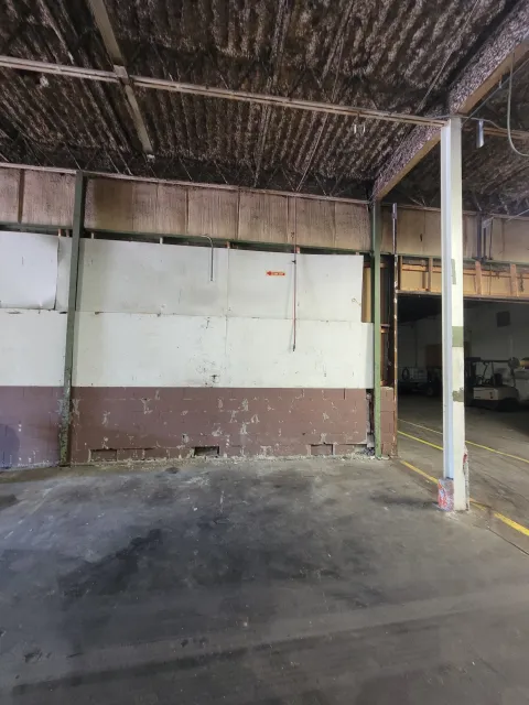 An empty indoor parking lot with worn concrete floor, a partially painted brick wall, and exposed ceiling beams.