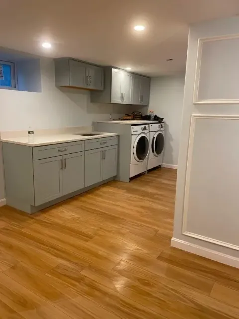 Basement laundry room with gray cabinets, washer and dryer, recessed lights, and wood floors