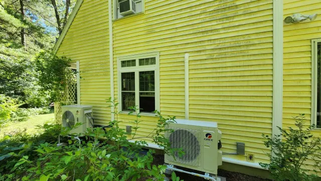 Yellow house exterior with green bushes, a window, and a Gree air conditioning unit outside.