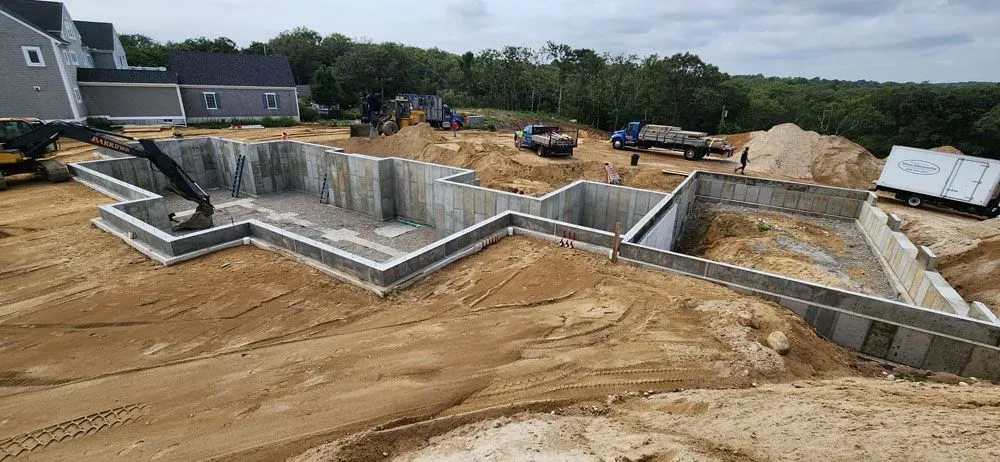 A large concrete base for a house is being built in a dirt field.