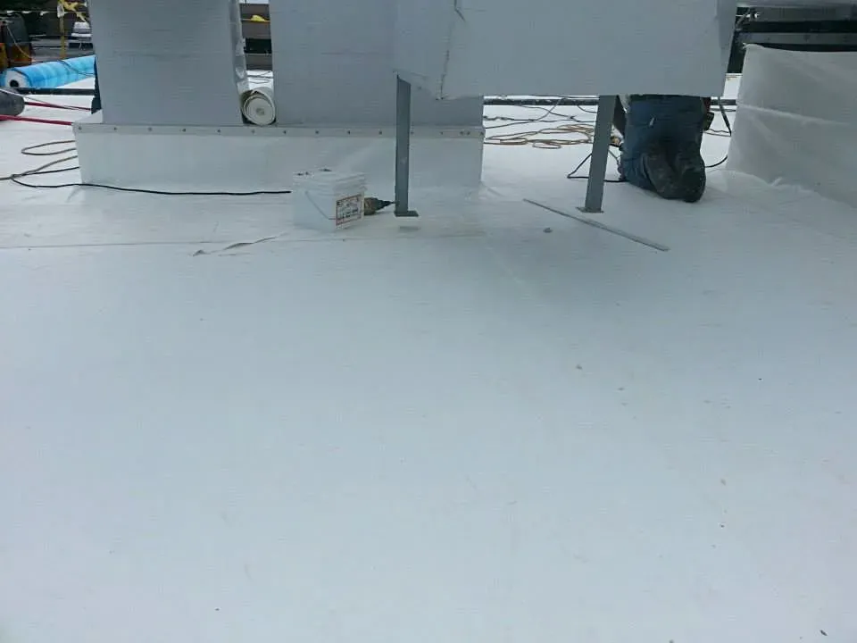 White flat roof being installed, with equipment and a worker's legs visible.
