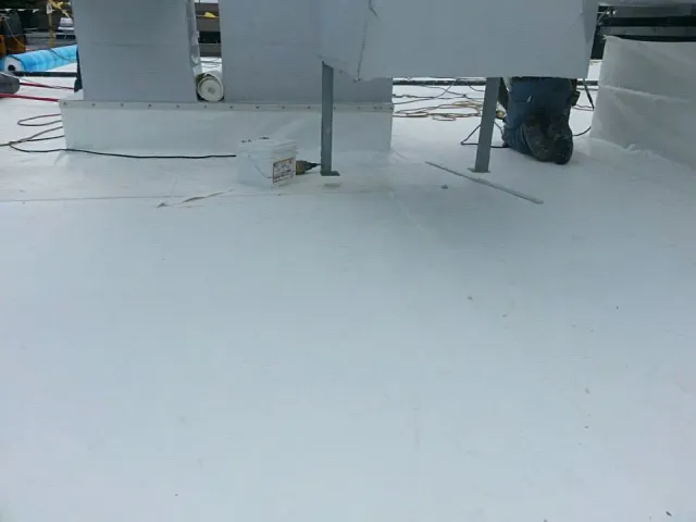 White flat roof being installed, with equipment and a worker's legs visible.