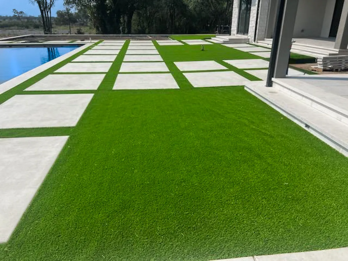 Modern backyard with concrete pavers and artificial grass grid layout next to a swimming pool.