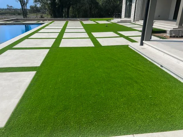 Modern backyard with concrete pavers and artificial grass grid layout next to a swimming pool.
