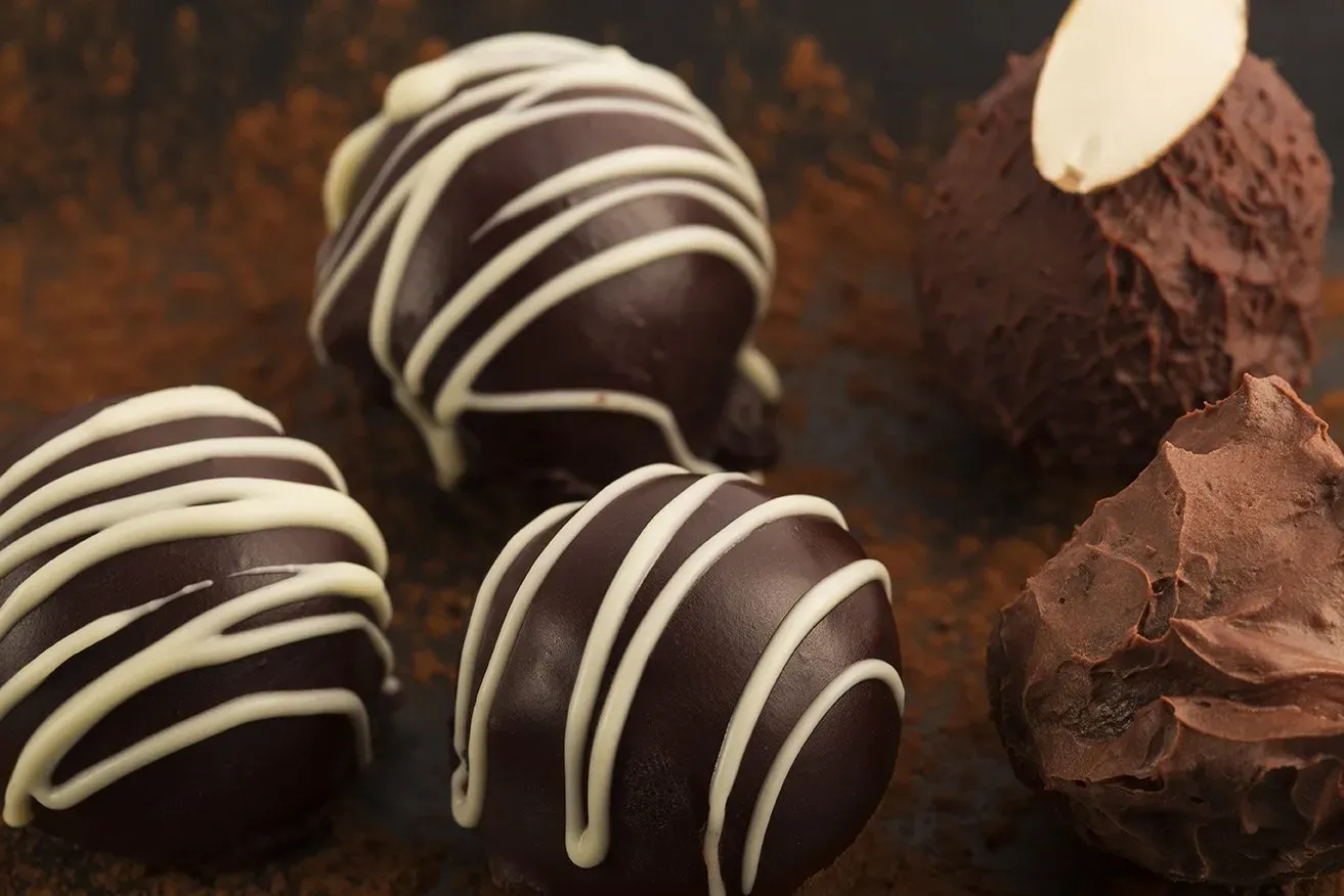 Chocolate truffles, some drizzled with white chocolate, arranged on a dark surface.